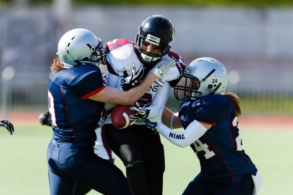Female football players tackling opponent on green field