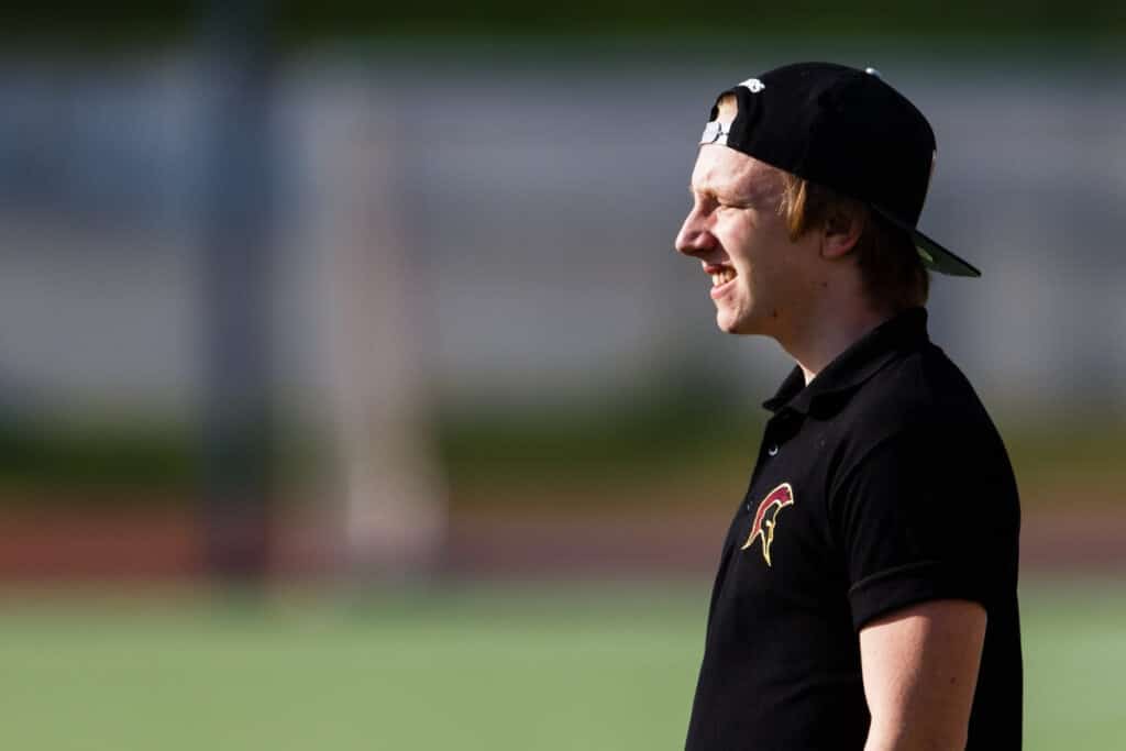 Man in black polo and cap smiling outdoors.