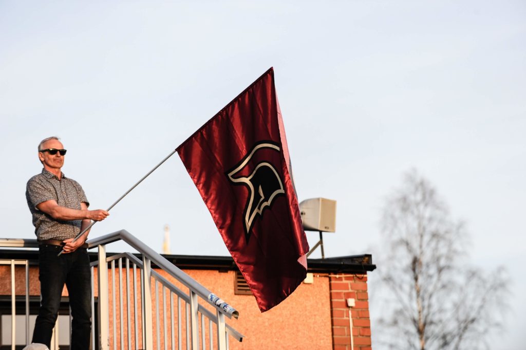 Mature man proudly holds large maroon flag.