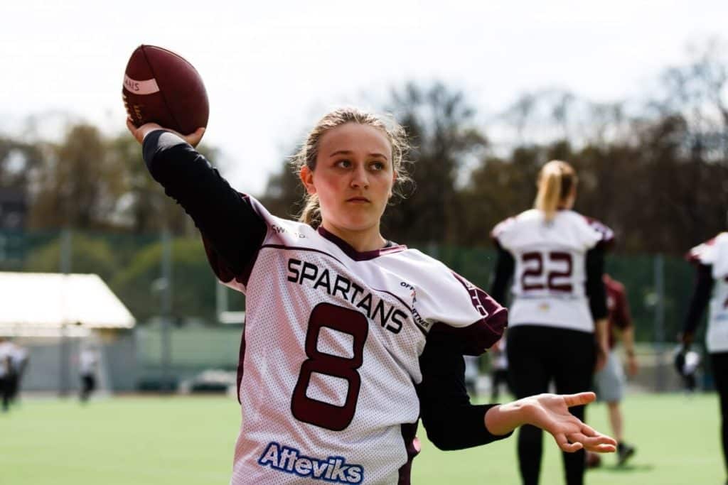 Athlete in Spartans uniform throws football on field.