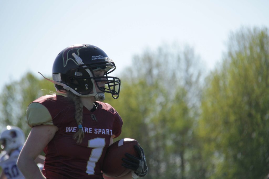 Female football player in maroon jersey holding ball.