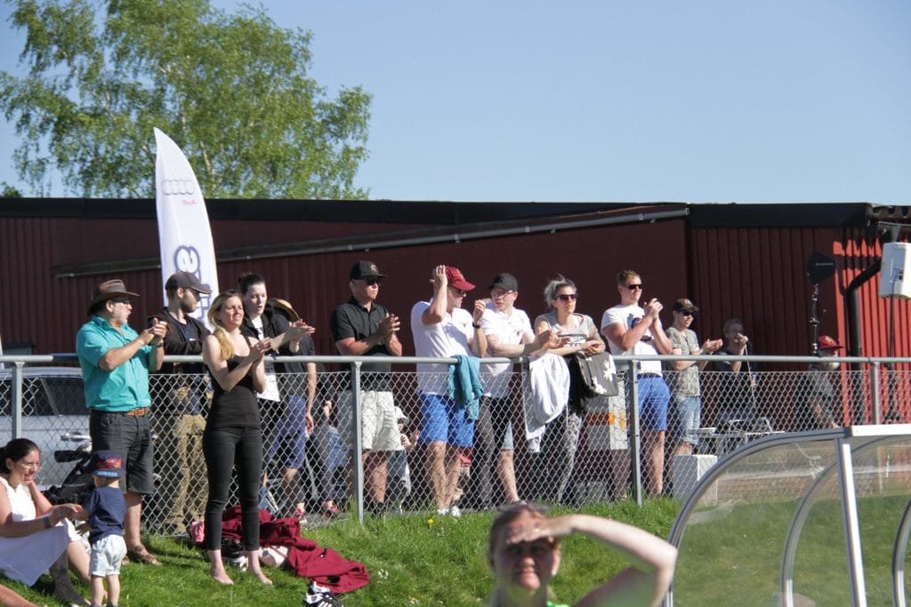 Outdoor spectators applaud standing by a red metal