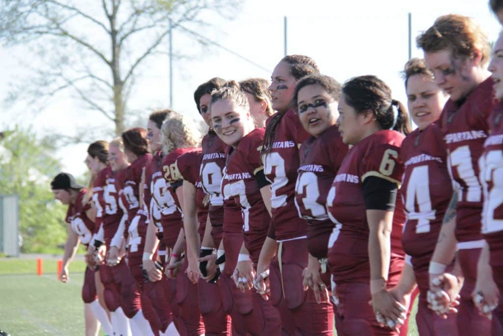 Women Spartans football players holding hands on field