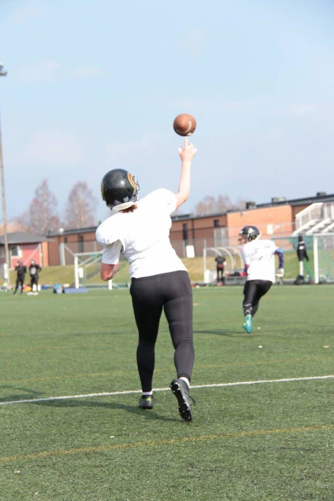 Player in white jersey throwing brown football outside