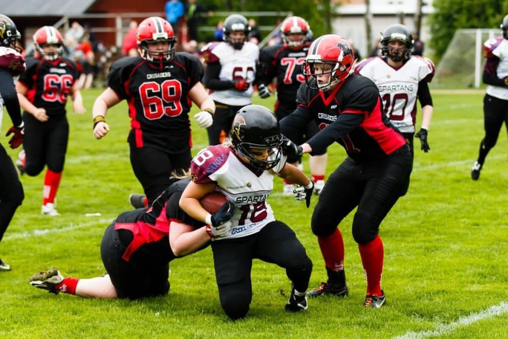 Intense female football players tackling on green field.