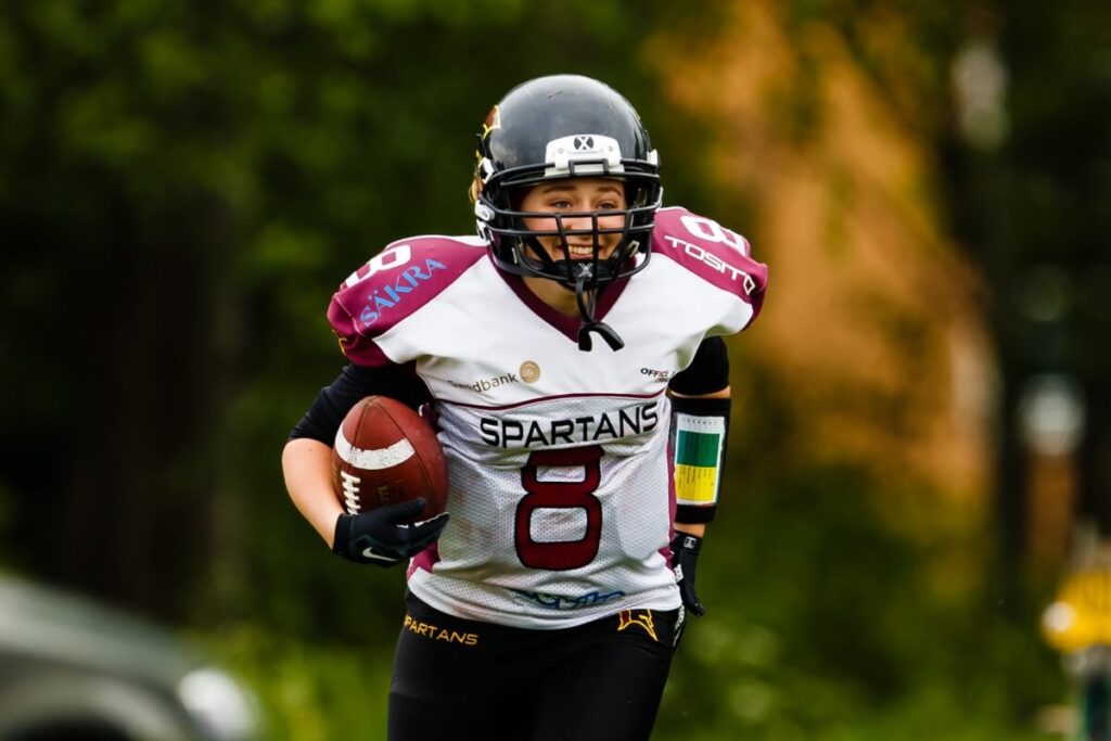 Female athlete running with football in SPARTANS jersey.