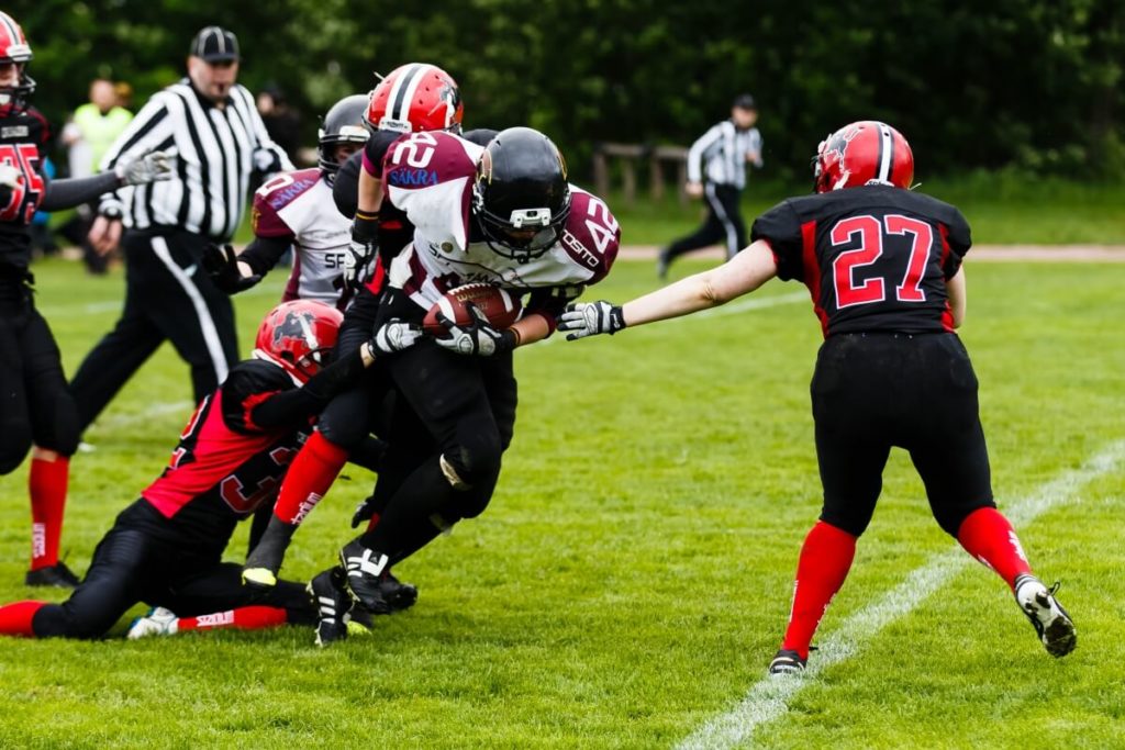 Football runner tackled by players on green sports