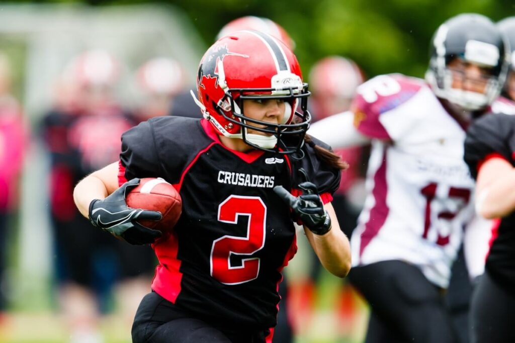 Female football player in red helmet running quickly.