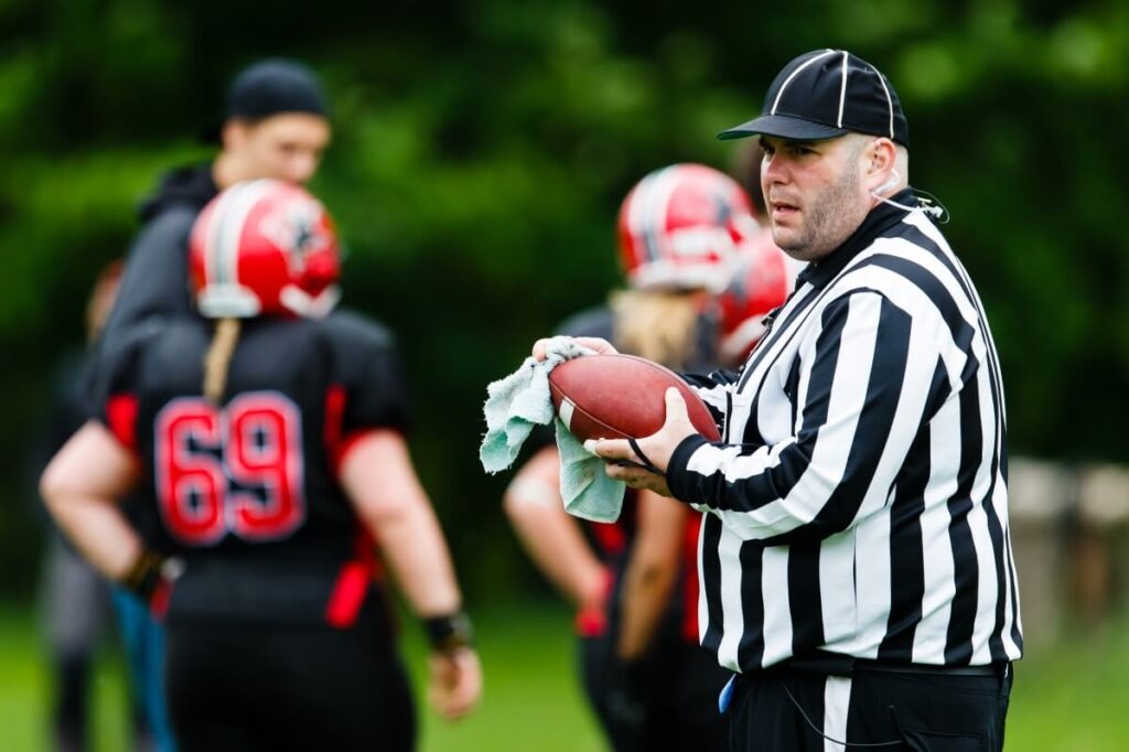 Football referee holding brown leather ball wiping sweat