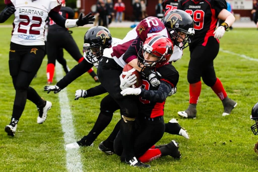 Football players tackle ball carrier on grassy field.