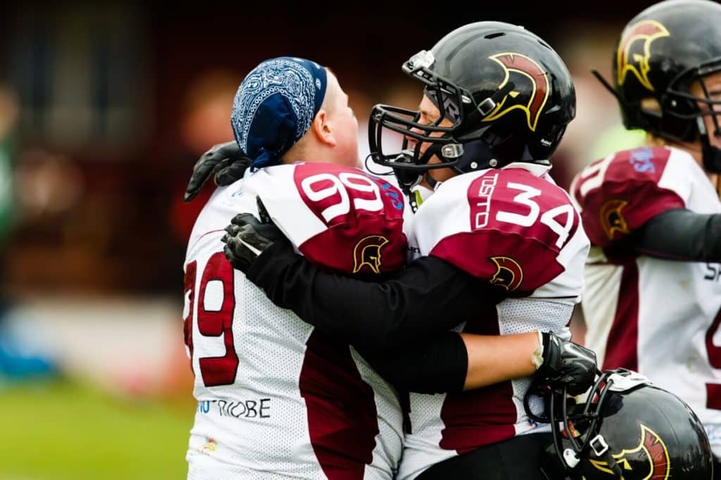 Football players hugging wearing white and maroon jerseys