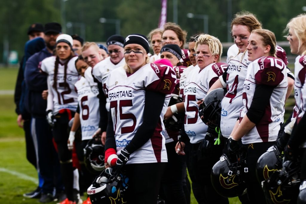 Serious women Spartans football team standing holding helmets