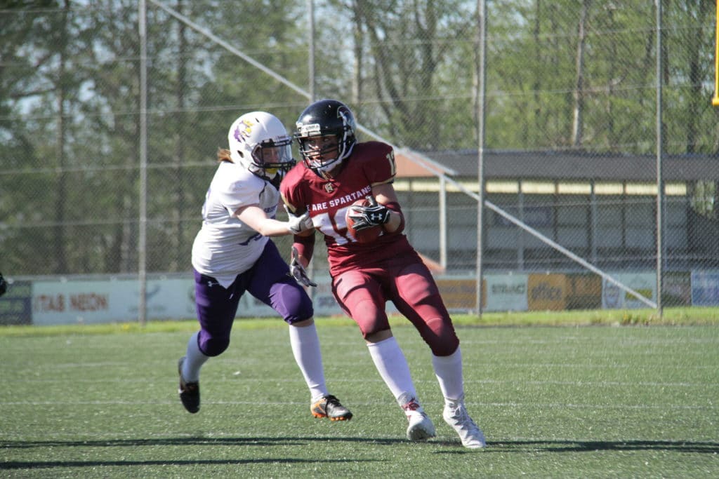 Maroon jersey runner evades white uniform football defender.