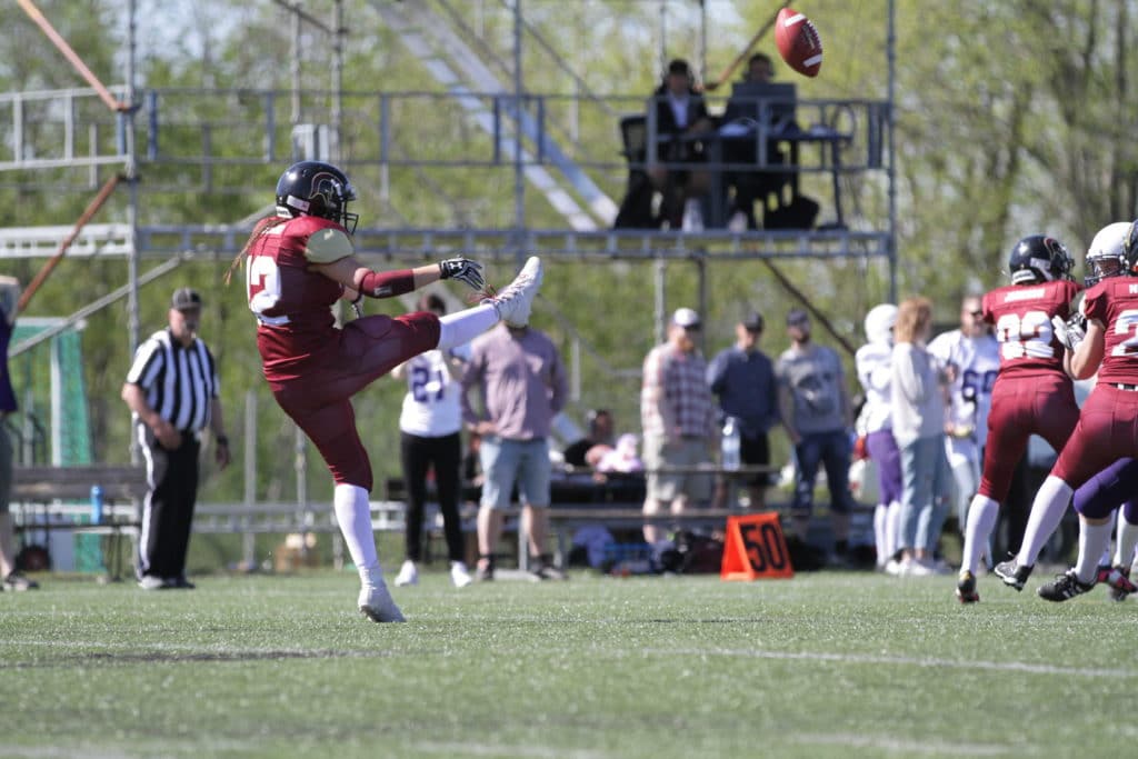 Maroon uniform player punting football on stadium field