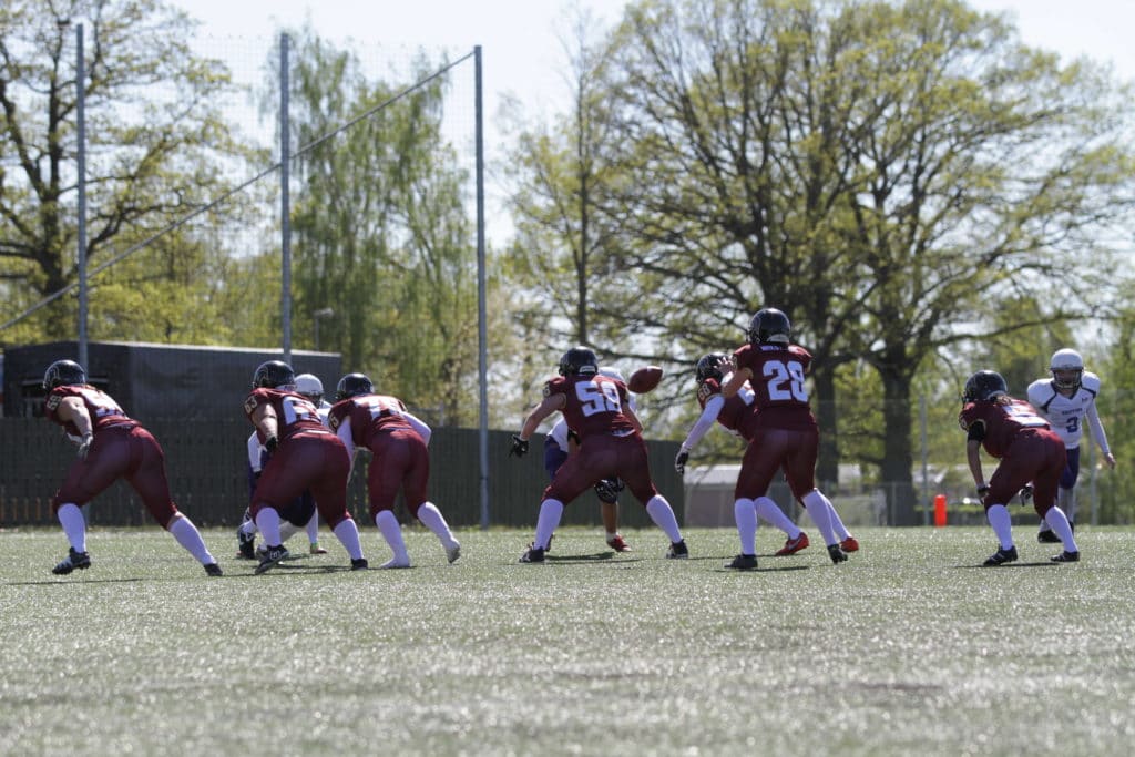Maroon football players scrimmage line outdoor turf field.