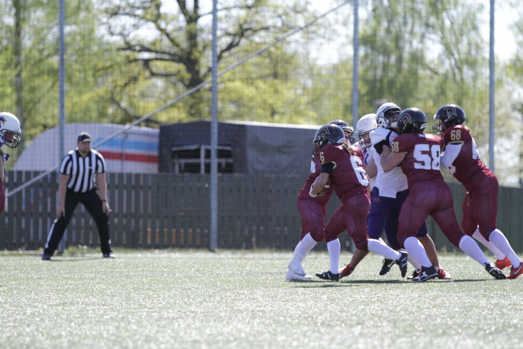 Maroon football players tackling opponent on turf field