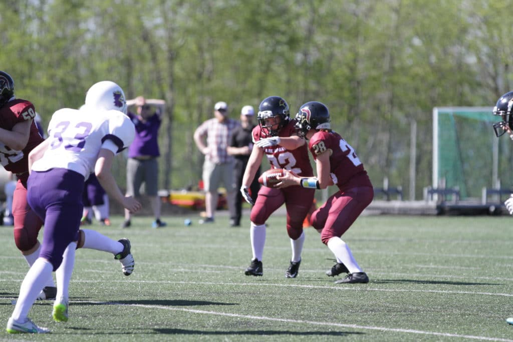 American football players scrimmage outdoors on green turf